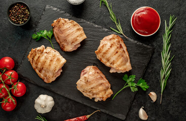 grilled skinless chicken thighs with spices and herbs on a stone background