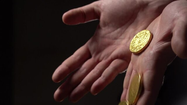 Gold Coins fall from the man's palms. Hands with gold coins on a black background. Slow motion. Close Up. Film grain