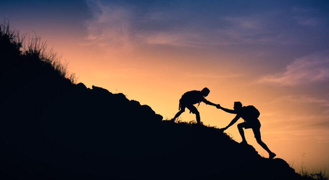 silhouette of a person on a mountain helping his friend giving him a helping hand. 