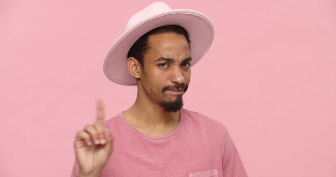 Young black man in pink hat grimacing and showing no gesture isolated over pink background