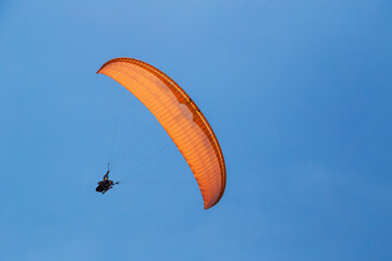 Tandem orange paragliding against a blue sky, sunny day