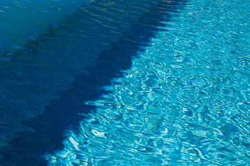 A two colored light and dark blue water with ripples and sunny reflections in a swimming pool.