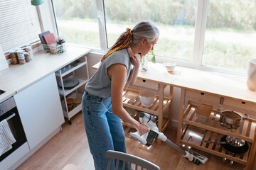 Mature female cleaning floor during smartphone conversation