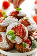 Close up view of muffins with strawberries sprinkled with powdered sugar and decorated with fresh mint leaves. Delicious breakfast or valentines dessert concept. 