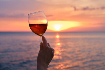 A glass of red wine in the hands of a girl in the rays of the sunset on the seashore. Alcoholic...