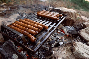 Grilling sausages on barbeque grill. Picnic in the forest.