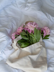 Vertical photo. A bouquet of pink peonies on white sheets in an eco-friendly eco cotton bag