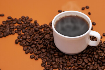 Warm cup of coffee and coffee beans on brown background. Coffee cup and coffee beans on the table