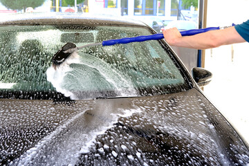 man washes his black car with water and foam at a self-service car wash, the concept of hygiene...