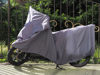 A motorcycle covered with an awning stands near a forged fence in the park