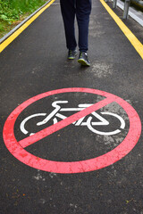 Obraz premium No cyclists on the asphalt pedestrian sidewalk in the foreground. In the background are the legs of a walking man in sneakers.