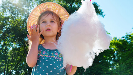 The girl looks in amazement and surprise at the amusement park. A child eats cotton candy on a...