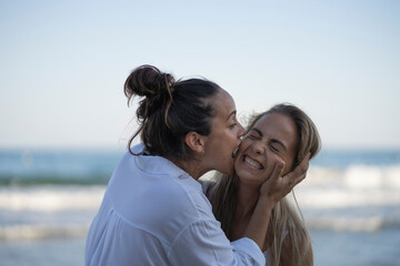 A couple of woman kissing and laughing on the beach on a summer day.
