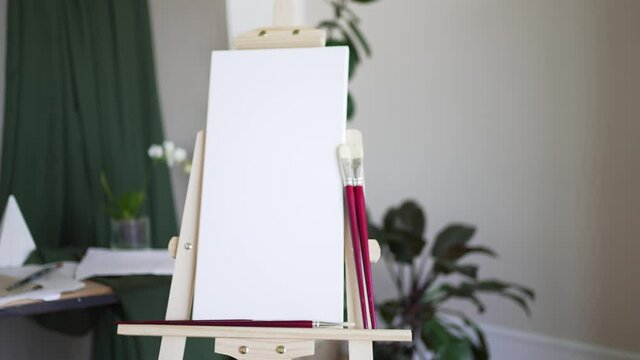 Creative studio. Empty white canvas on a wooden easel and red brushes