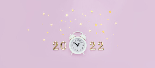 Numbers 2022 and white alarm clock are decorated with star confetti on pink background. Minimal New Year concept. Top view, banner