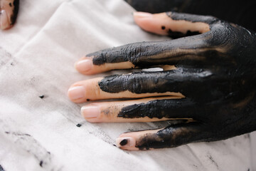 Whole body mud wrap. The hand is covered with a clay mask. Spa procedure in a luxury salon. Black clay Application. Skin cleansing and joint treatment. Health and beauty scrub. Relaxation and pleasure