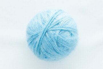 One round ball of blue color in the center of the frame on a white woven background on the theme of hand-made hobby knitting