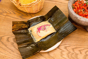 Mexican tamale of cochinita pibil stewed inside corn cob leaf with volcanic stone molcajete filled...