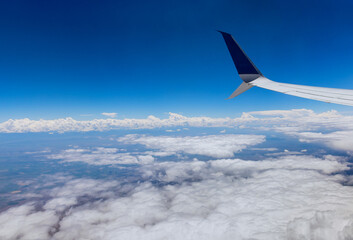 Fototapeta premium Airplane wing view out of the window on the cloudy sky the earth background