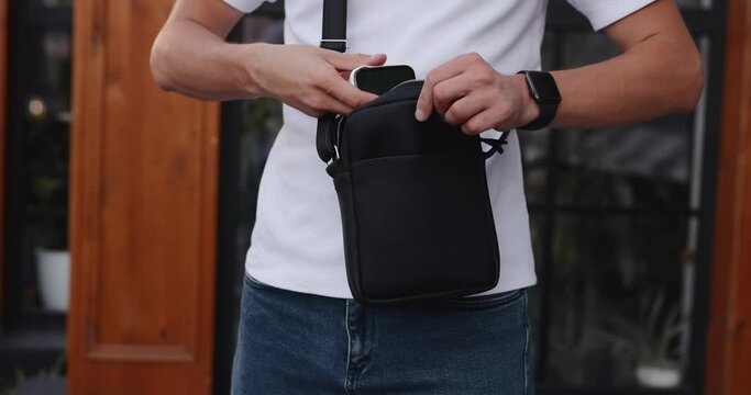 Unrecognizable man puts a mobile phone into the messenger bag, closeup