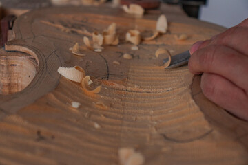 Luthier's hands using gouge to work the wood and make a violin