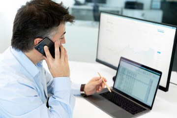 Stock broker businessman analyzing graphs and charts and talking by phone