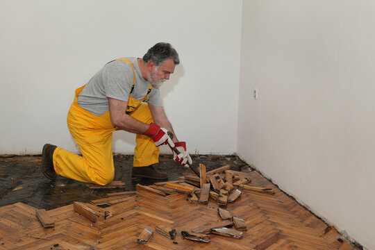 Worker removing old damaged parquet using crowbar tool