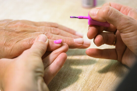 A manicurist applies pink gel shellac nail polish with a brush on a client's nails in a beauty salon. Spa treatments. Women's hands and fingers at the wooden table up close. Female nail care process.