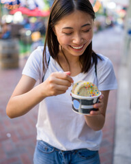 Happy Young Asian Woman Wearing Distressed Jeans and T-Shirt Eating an Ice Cream Sandwich in a Downtown Urban Area