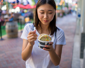 Happy Young Asian Woman Wearing Distressed Jeans and T-Shirt Eating an Ice Cream Sandwich in a Downtown Urban Area