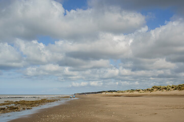 Landscape of a beach with some people walking and wide blue sky with white cotton clouds