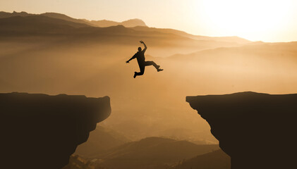 Silhouette jumping cliff sunset mountain. Courageous Man Jump Between Two Cliffs. Business Goals achievement concept 