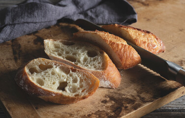 Cutting a baguette with a knife, placed on an old wooden cutting board.