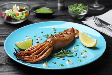 Delicious grilled squid served on black wooden table, closeup