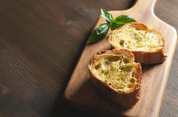 Sliced baked bread with garlic and herbs on a wooden cutting board on the table.