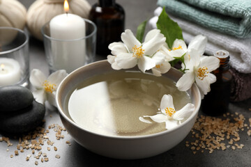Beautiful spa composition with jasmine essential oil and fresh flowers on grey table, closeup