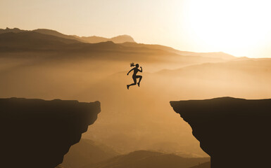 Businesswoman Goal and success concept Idea.
Girl Jumping Over the Cliff in Mountain Sunset background. Brave and Courageous Young Woman Jumps between two Cliffs In Front Of The Sun. Superpower Female