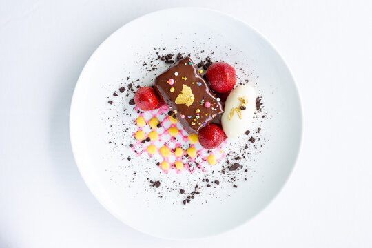 Chocolate Bar Dessert With Strawberries & A White Chocolate Egg With Oreo Cookie Crumble Served On White Plate. Overhead Shot