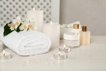 Composition with beautiful jasmine flowers and burning candles on white wooden table