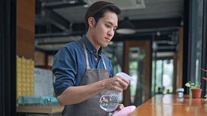Young waiter cleaning  tables with sanitizer spray  at coffee shop
