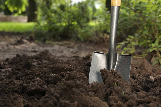 Shovel in soil outdoors, space for text. Gardening tool