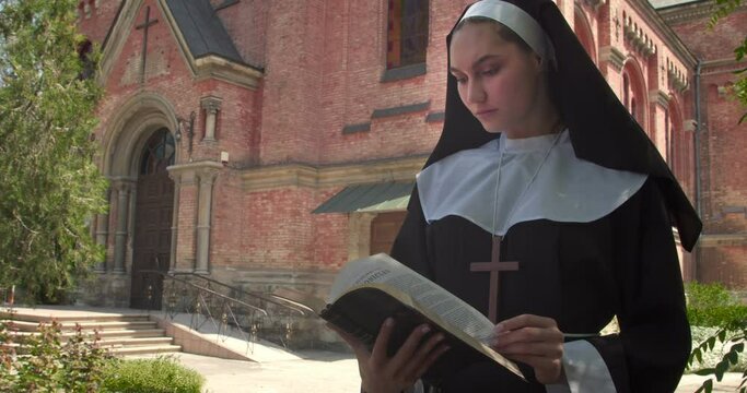 Young nun reading Bible outdoors near monastery