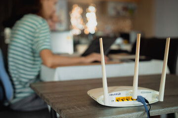 A woman is working at home using a modem router, connecting the Internet to her laptop. - obrazy, fototapety, plakaty