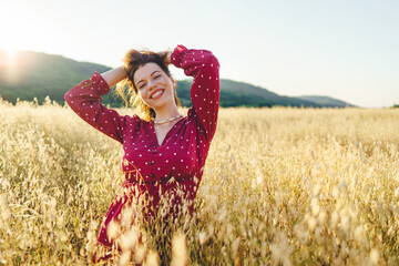 Portrait of adult caucasian brunette woman wearing red dress in summer day standing in the crops grain field smiling happy looking to the camera with copy space