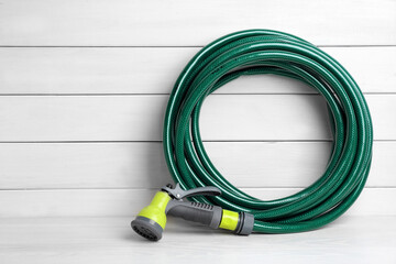 Green garden hose with spray gun on white wooden table, space for text