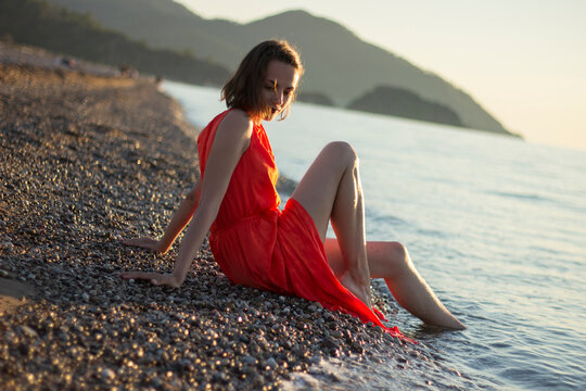 stylish beautiful girl in a red dress sitting and posing at sunset