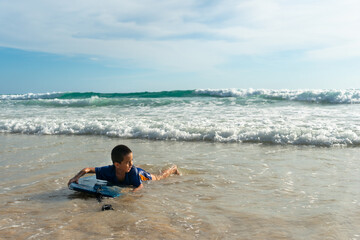 Fototapeta na wymiar A boy lay down on body board while the wave move to the beach..Paradise beach blue sea, and clear sand landscape. .waves crashing on the beach background..smiling face of happy boy relax concept.