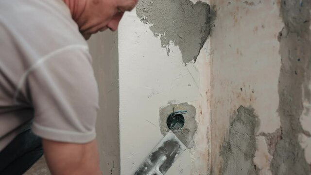 Male plasterer in protective gloves putting spackling paste on metal spatula for aligning cement walls and sealing holes on construction site, builder using putty stucco for apartment interior