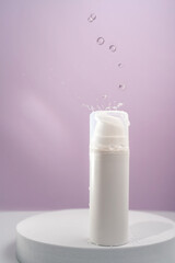 Cosmetic bottle with water splashes on a purple background.