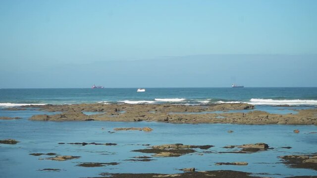 Three ships in the ocean, view from far away with rocks and waves close to the image